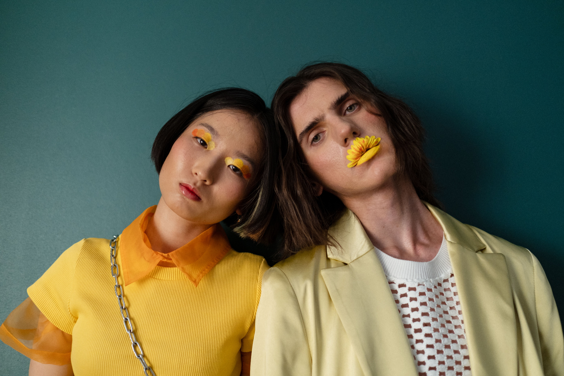Two people in yellow, leaning head-to-head against a teal wall